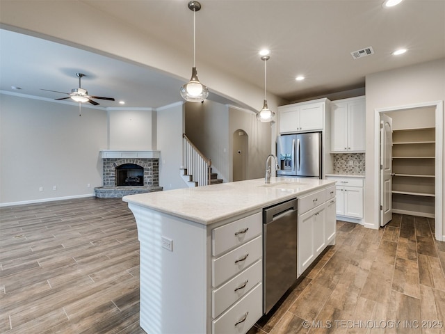 kitchen with decorative light fixtures, white cabinets, a center island with sink, and stainless steel appliances