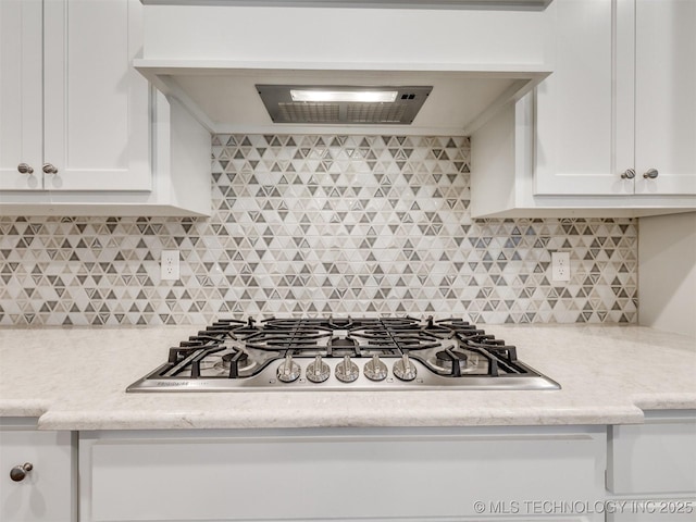 kitchen featuring tasteful backsplash, stainless steel gas stovetop, premium range hood, light stone countertops, and white cabinets