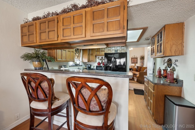 kitchen featuring a textured ceiling, a kitchen bar, black refrigerator with ice dispenser, kitchen peninsula, and light wood-type flooring