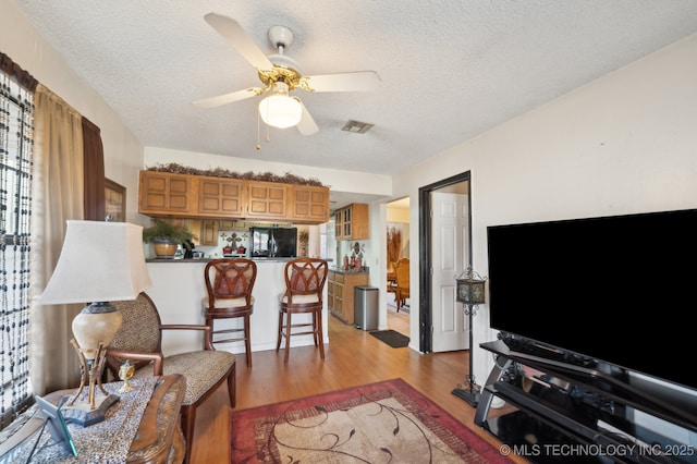 living room with ceiling fan, light hardwood / wood-style floors, and a textured ceiling