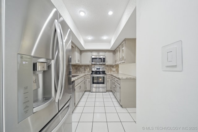 kitchen featuring a textured ceiling, a tray ceiling, stainless steel appliances, backsplash, and light tile patterned floors