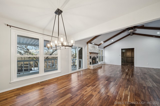 unfurnished dining area with hardwood / wood-style flooring, ceiling fan with notable chandelier, a stone fireplace, and lofted ceiling with beams