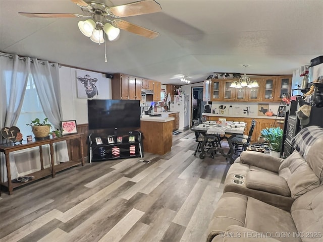 living room with ceiling fan with notable chandelier, light wood-type flooring, and vaulted ceiling