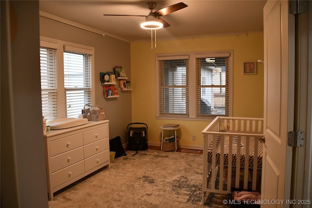 bedroom featuring ceiling fan, a nursery area, crown molding, and light carpet