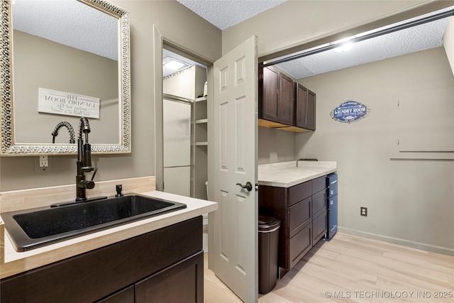 clothes washing area featuring light hardwood / wood-style floors, sink, and a textured ceiling