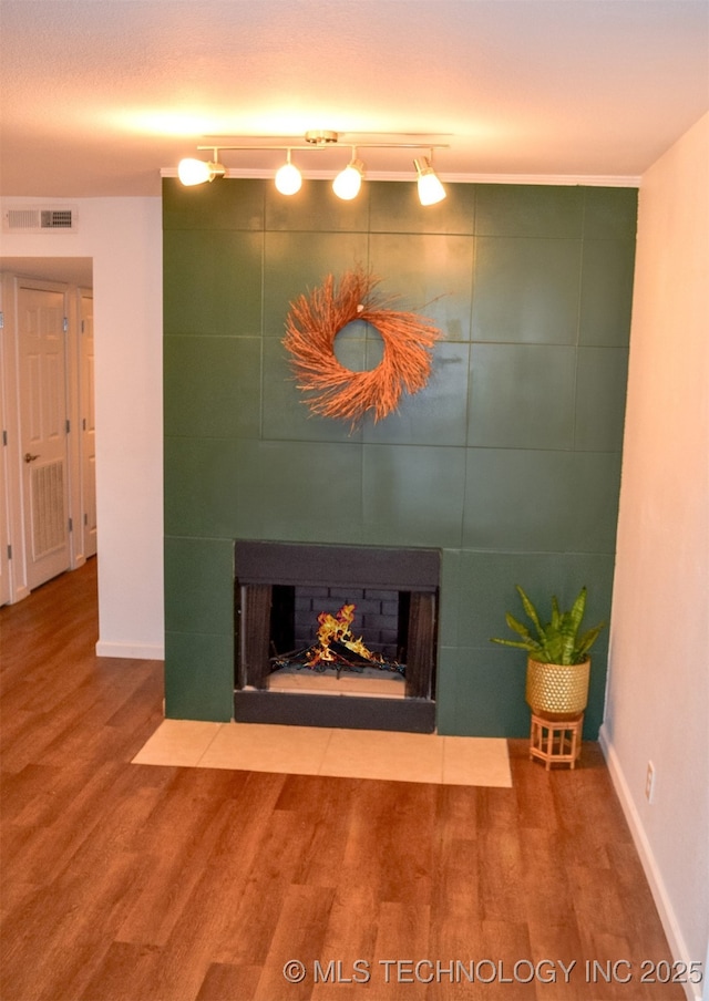 unfurnished living room with a fireplace, wood finished floors, visible vents, and baseboards