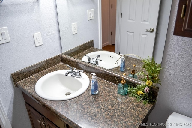 half bathroom with toilet, a textured wall, and vanity