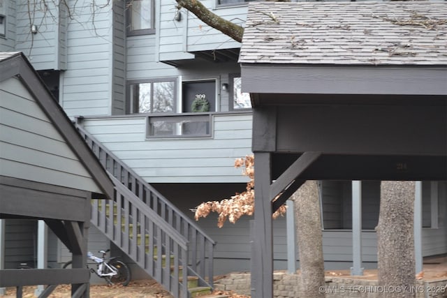 view of side of home with roof with shingles and stairway