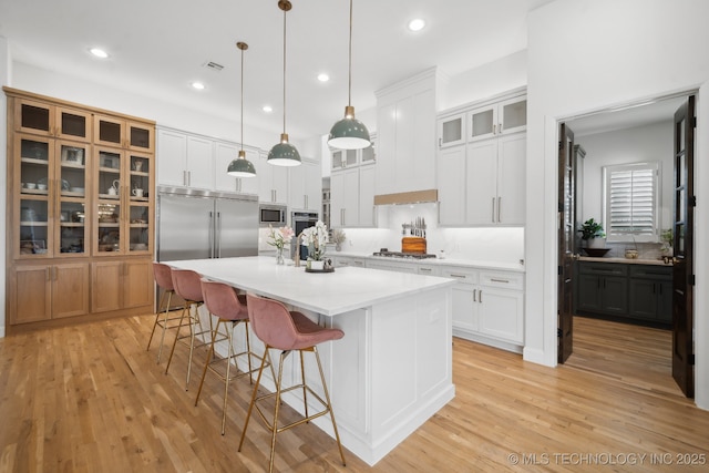 kitchen featuring white cabinetry, pendant lighting, a center island with sink, and built in appliances