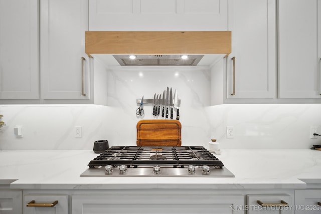 interior space featuring stainless steel gas cooktop, white cabinetry, light stone countertops, and premium range hood