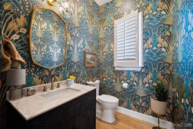 bathroom featuring vanity, toilet, baseboards, wallpapered walls, and wood finished floors