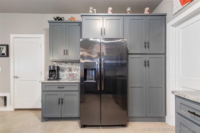 kitchen with light stone countertops, gray cabinetry, stainless steel fridge, and decorative backsplash