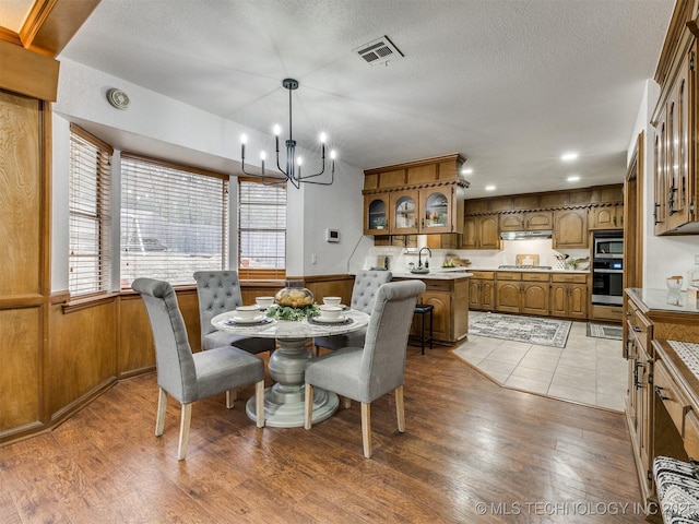 dining room with a textured ceiling, hardwood / wood-style floors, an inviting chandelier, and wooden walls