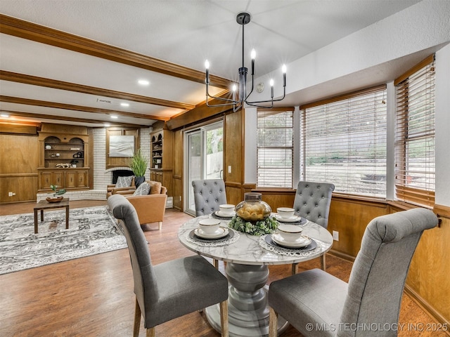 dining room featuring a fireplace, a chandelier, light wood-type flooring, built in shelves, and wood walls