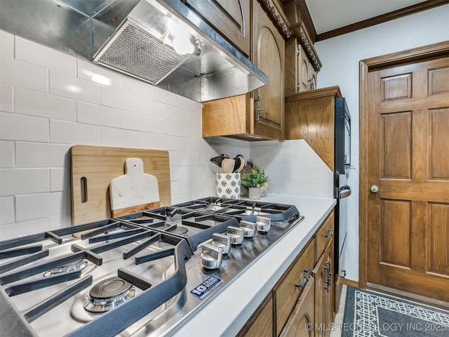 kitchen with exhaust hood, ornamental molding, stainless steel gas cooktop, and tasteful backsplash