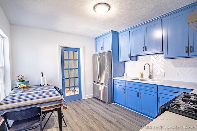 kitchen with decorative backsplash, sink, stainless steel fridge, light wood-type flooring, and blue cabinets