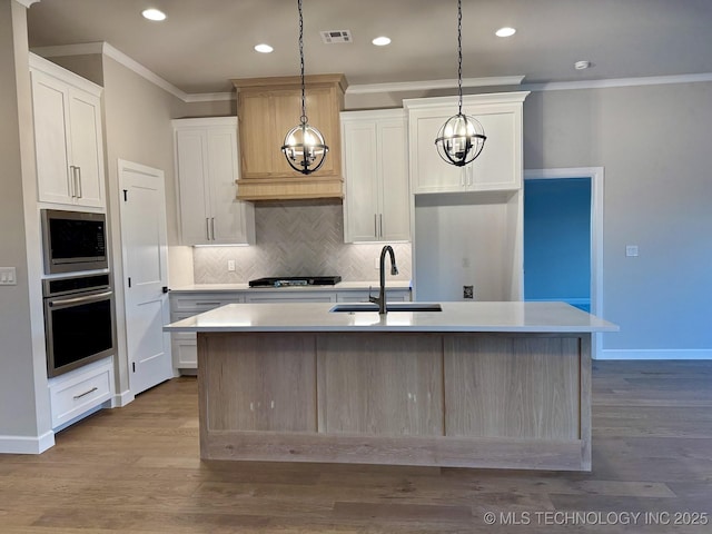 kitchen with pendant lighting, sink, appliances with stainless steel finishes, white cabinetry, and a center island with sink