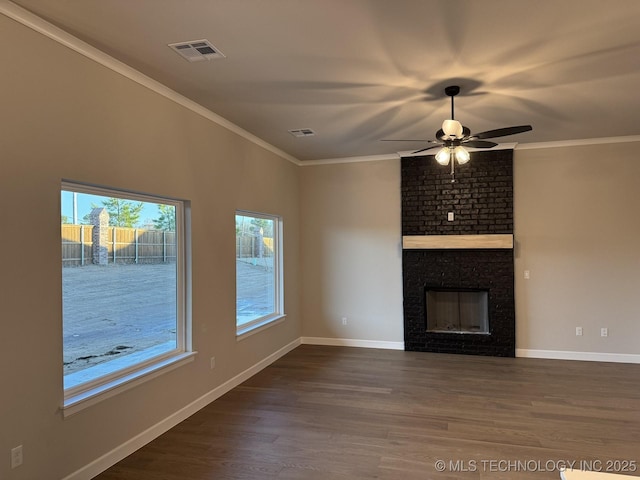 unfurnished living room with ornamental molding, a brick fireplace, dark wood-type flooring, and plenty of natural light