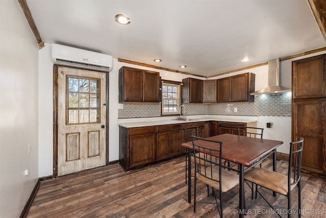 kitchen with dark brown cabinets, sink, dark hardwood / wood-style floors, wall chimney range hood, and a wall mounted AC