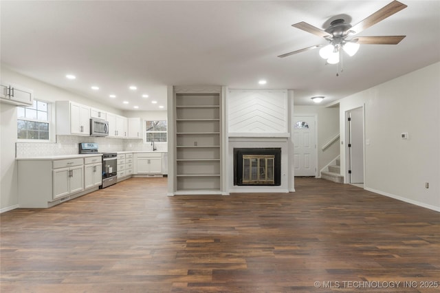 unfurnished living room featuring a fireplace, dark hardwood / wood-style flooring, ceiling fan, and a healthy amount of sunlight