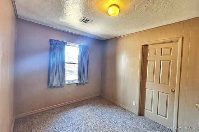 spare room featuring a textured ceiling, wood walls, and carpet flooring