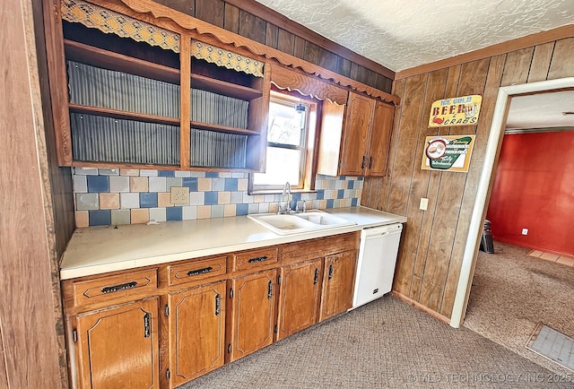 kitchen featuring a textured ceiling, carpet, dishwasher, wooden walls, and sink