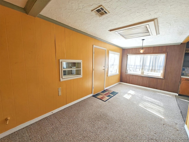 carpeted empty room with a textured ceiling, wood walls, and beamed ceiling