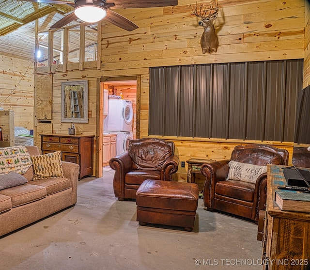 living room featuring ceiling fan, a towering ceiling, stacked washing maching and dryer, concrete floors, and wood walls