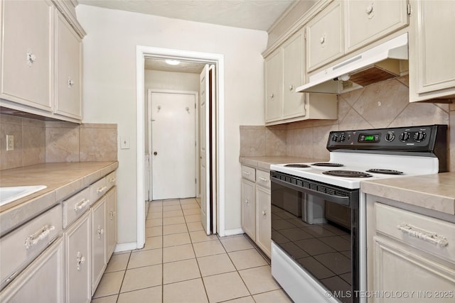 kitchen featuring light tile patterned flooring, cream cabinetry, backsplash, and electric range