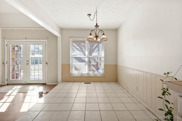 doorway to outside featuring light tile patterned floors, a notable chandelier, french doors, and a textured ceiling