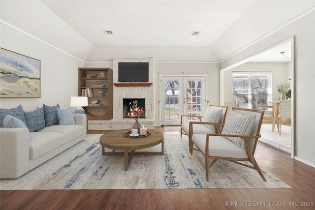 living room featuring a stone fireplace, vaulted ceiling, and wood-type flooring