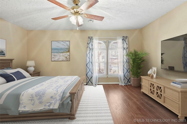 bedroom with ceiling fan, dark hardwood / wood-style flooring, and a textured ceiling