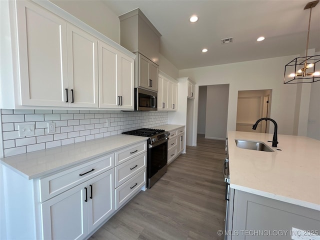 kitchen with a sink, appliances with stainless steel finishes, white cabinetry, light wood finished floors, and decorative backsplash
