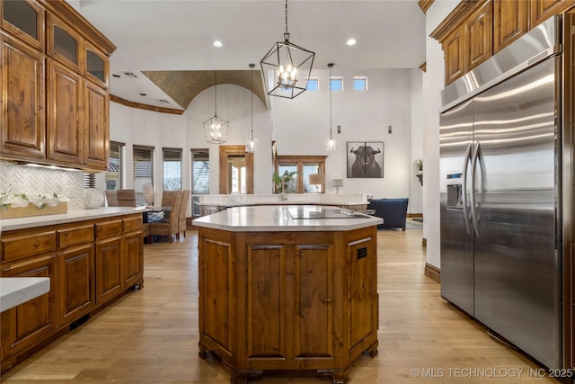 kitchen featuring built in fridge, hanging light fixtures, light wood-type flooring, a kitchen island, and backsplash