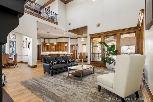 living room with a towering ceiling, crown molding, and light hardwood / wood-style floors