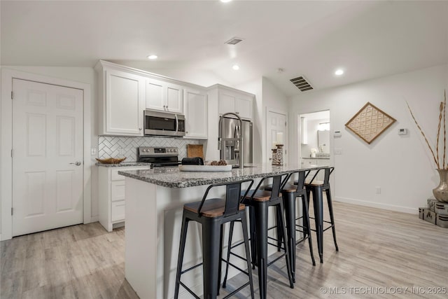 kitchen with a center island with sink, white cabinets, vaulted ceiling, and appliances with stainless steel finishes