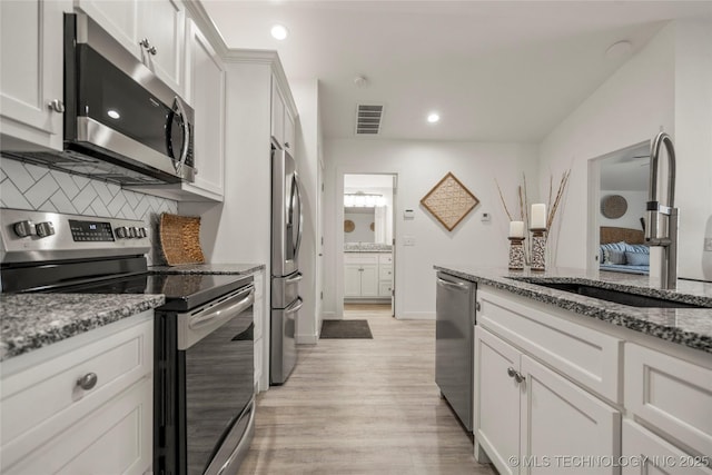 kitchen with white cabinetry, stainless steel appliances, sink, stone countertops, and light hardwood / wood-style flooring