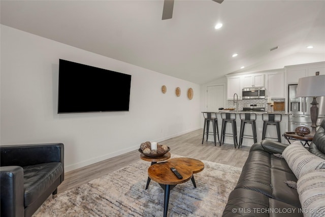 living room featuring ceiling fan, light hardwood / wood-style floors, sink, and lofted ceiling