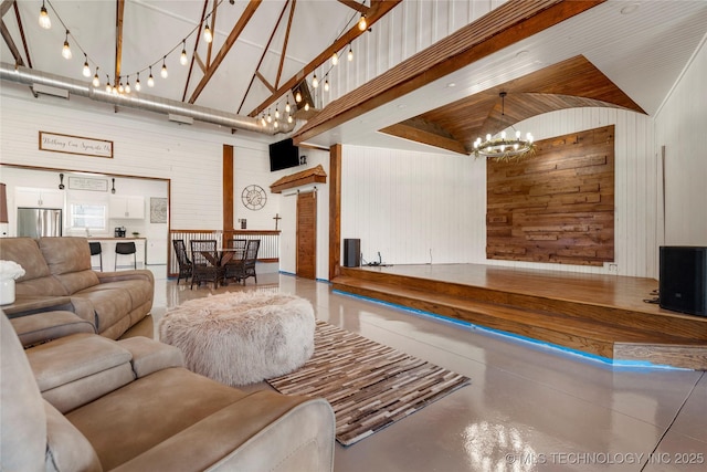 living room with a chandelier, wooden walls, concrete flooring, and high vaulted ceiling