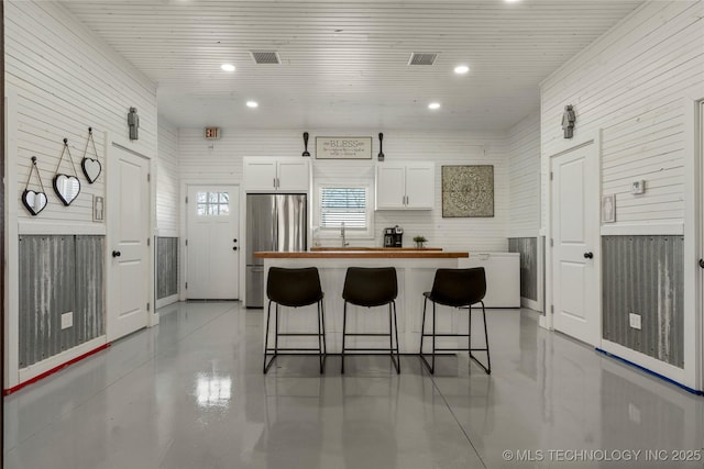 kitchen featuring white cabinets, a center island, a kitchen bar, wooden walls, and stainless steel fridge