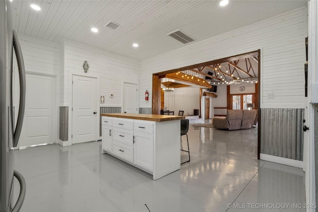 kitchen featuring white cabinets, butcher block counters, stainless steel fridge, wood walls, and a breakfast bar area