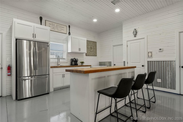 kitchen featuring white cabinets, a center island, wood counters, a kitchen breakfast bar, and stainless steel refrigerator