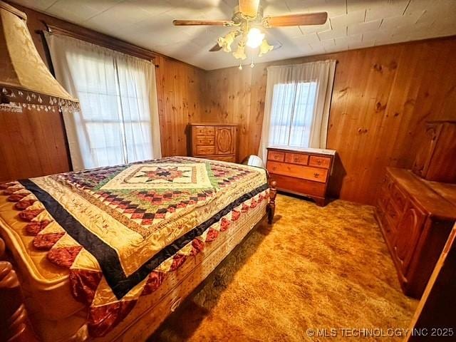 bedroom with ceiling fan, wood walls, and carpet flooring