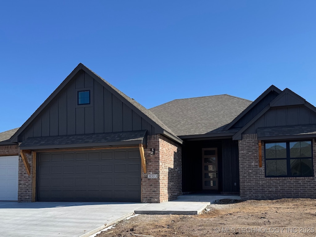 view of front of home featuring a shingled roof, a garage, brick siding, and board and batten siding