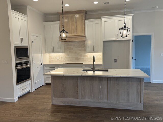 kitchen featuring white cabinets, a kitchen island with sink, pendant lighting, and oven