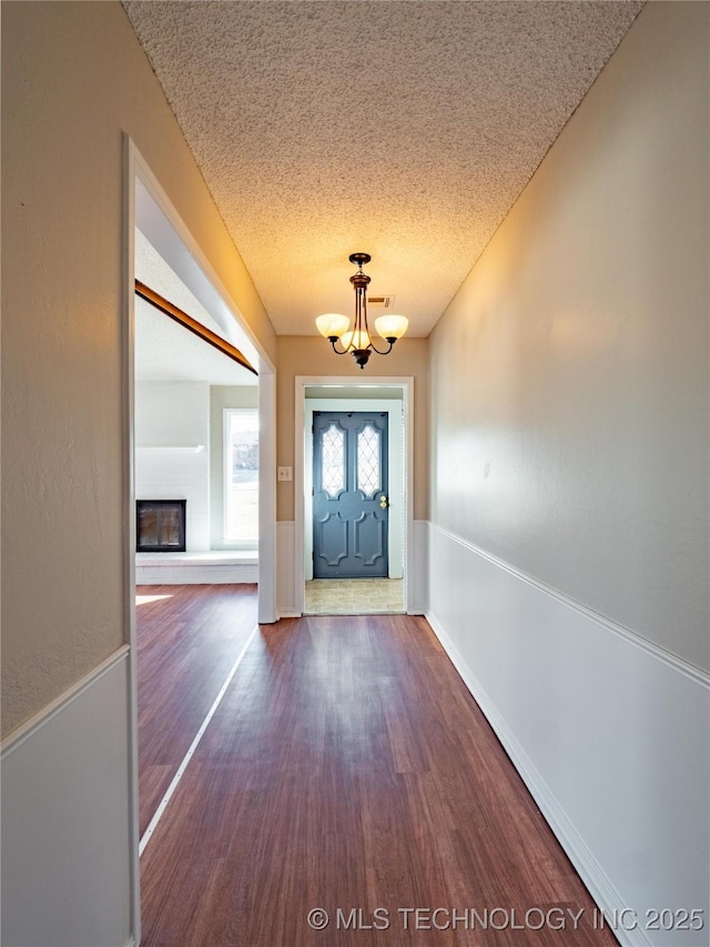 doorway to outside featuring dark wood-type flooring, a textured ceiling, and an inviting chandelier