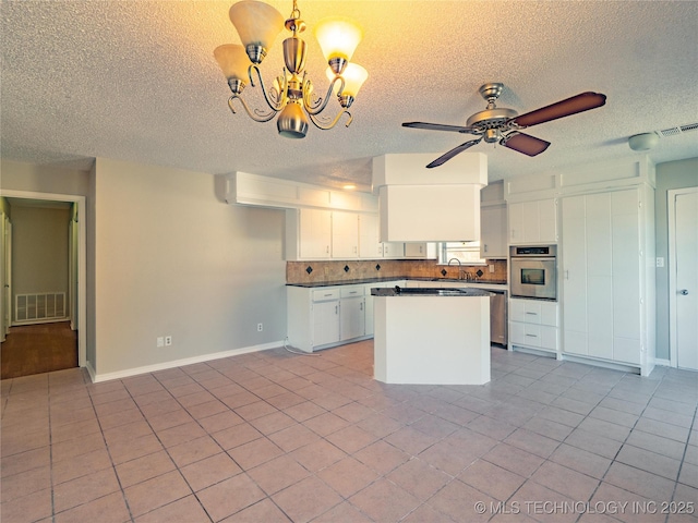 kitchen with stainless steel oven, tasteful backsplash, white cabinets, sink, and decorative light fixtures