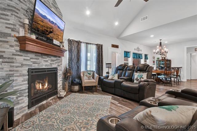 living room featuring hardwood / wood-style flooring, ceiling fan with notable chandelier, high vaulted ceiling, and a fireplace