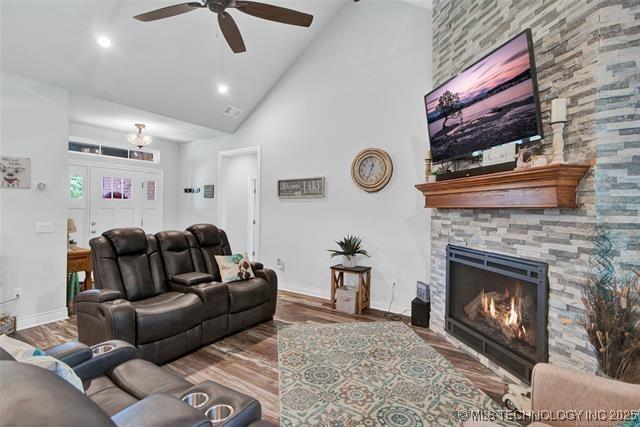 living room featuring ceiling fan, high vaulted ceiling, wood-type flooring, and a stone fireplace