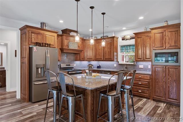 kitchen featuring pendant lighting, light stone countertops, a kitchen island, decorative backsplash, and stainless steel appliances